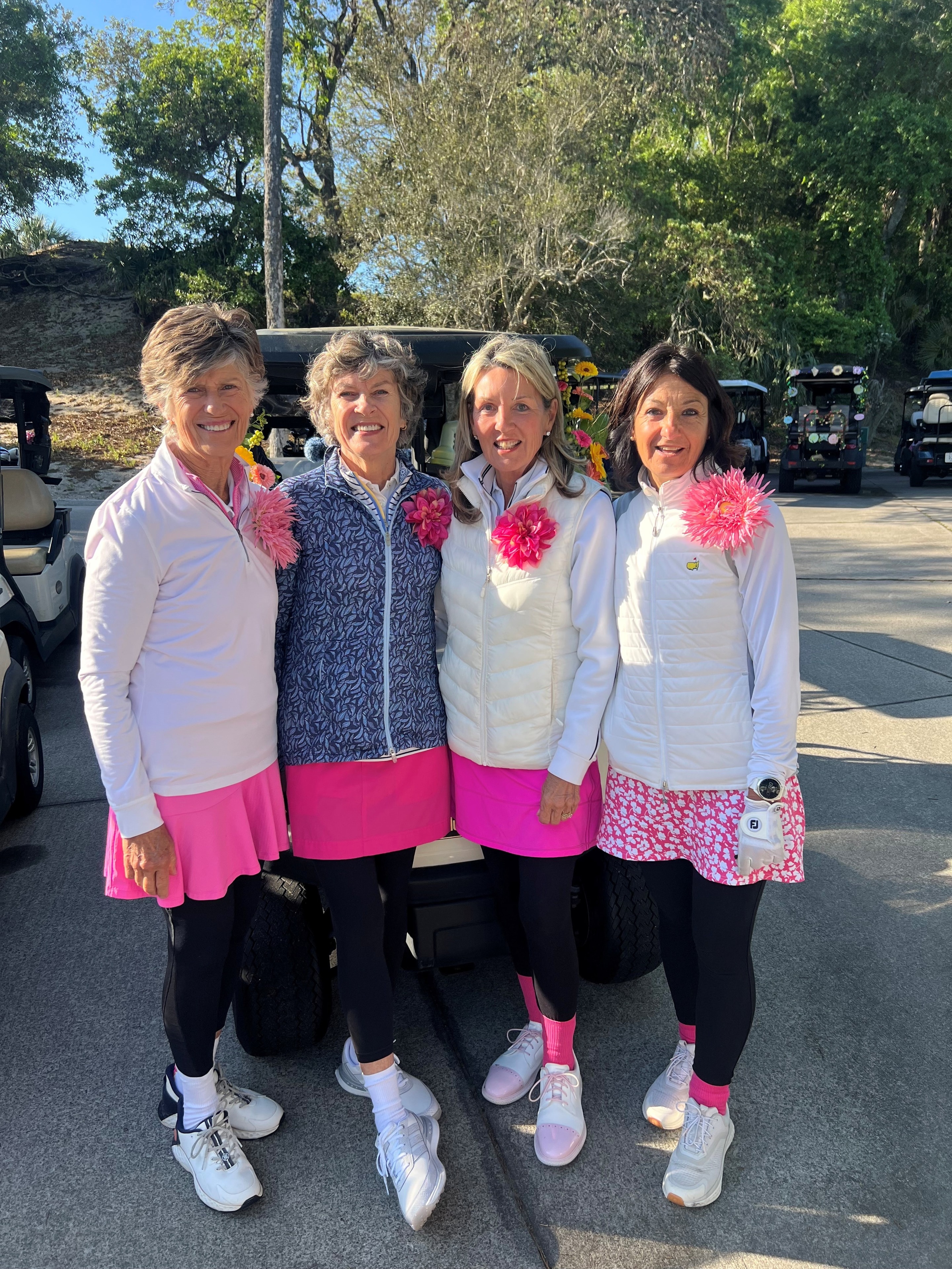 Four Wild Dunes LGA ladies in pink outfits with flower corsages by the golf carts