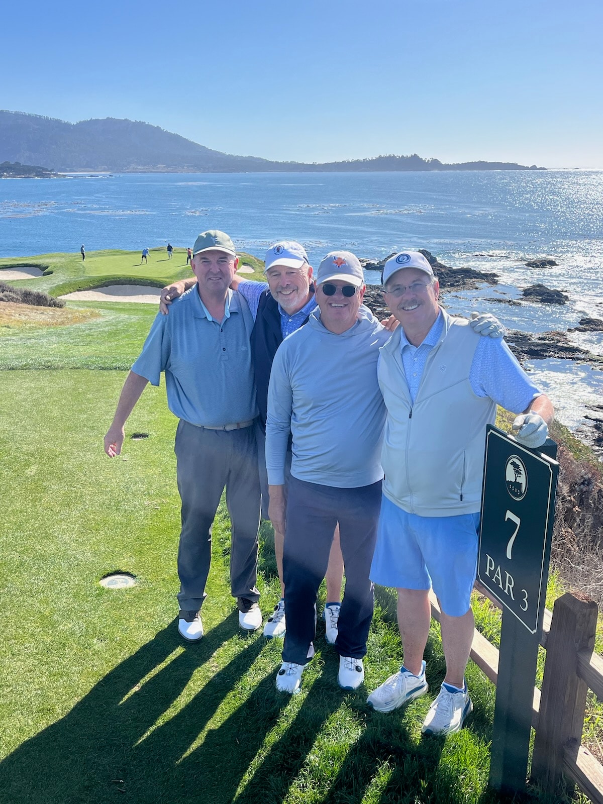 Four Wild Dunes members at Pebble Beach Hole 7 Par 3 with the Pacific Ocean behind them